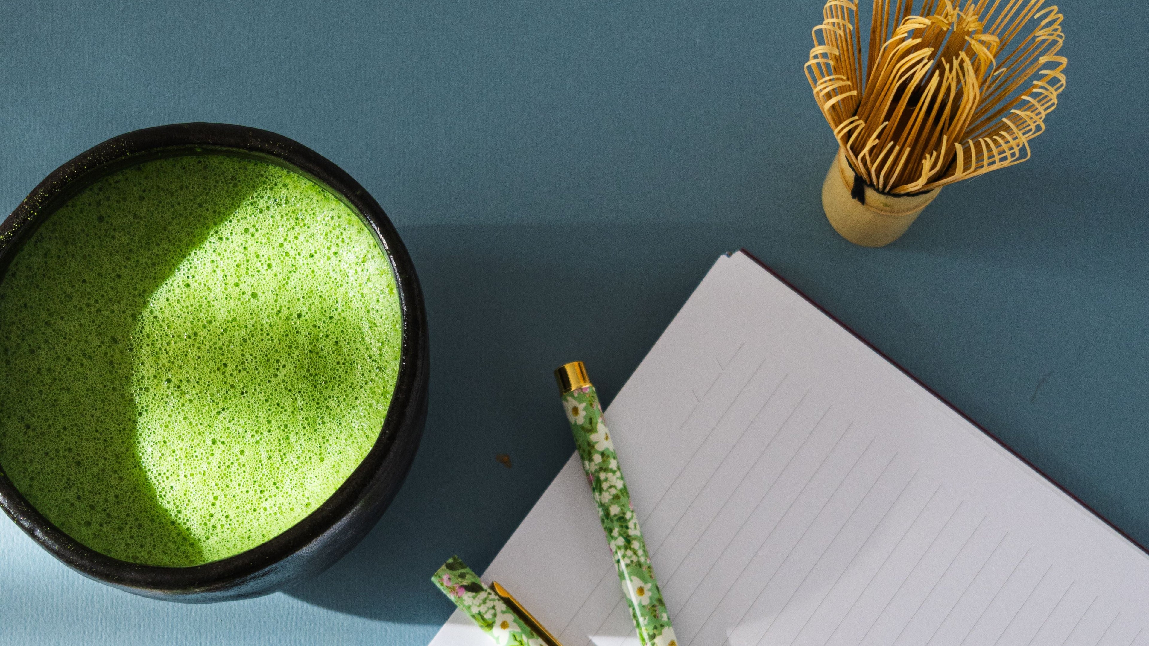Matcha green tea bowl,Uji packaging, and stationery on a blue surface